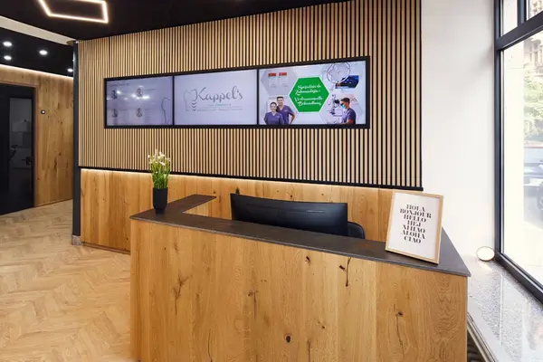 Modern eingerichteter Empfangsbereich einer Zahnarztpraxis mit Holzdekor und Digitalanzeige.
