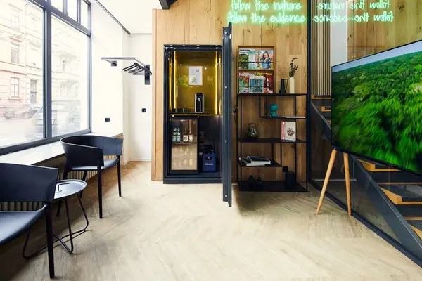 Moderner Wartebereich mit schwarzen Stühlen, Minibar, Zeitschriftenregal und Fernseher.