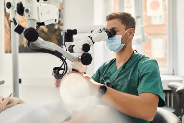 Zahnarzt untersucht Patienten mit Mikroskop in moderner Zahnarztpraxis für Wurzelbehandlung.